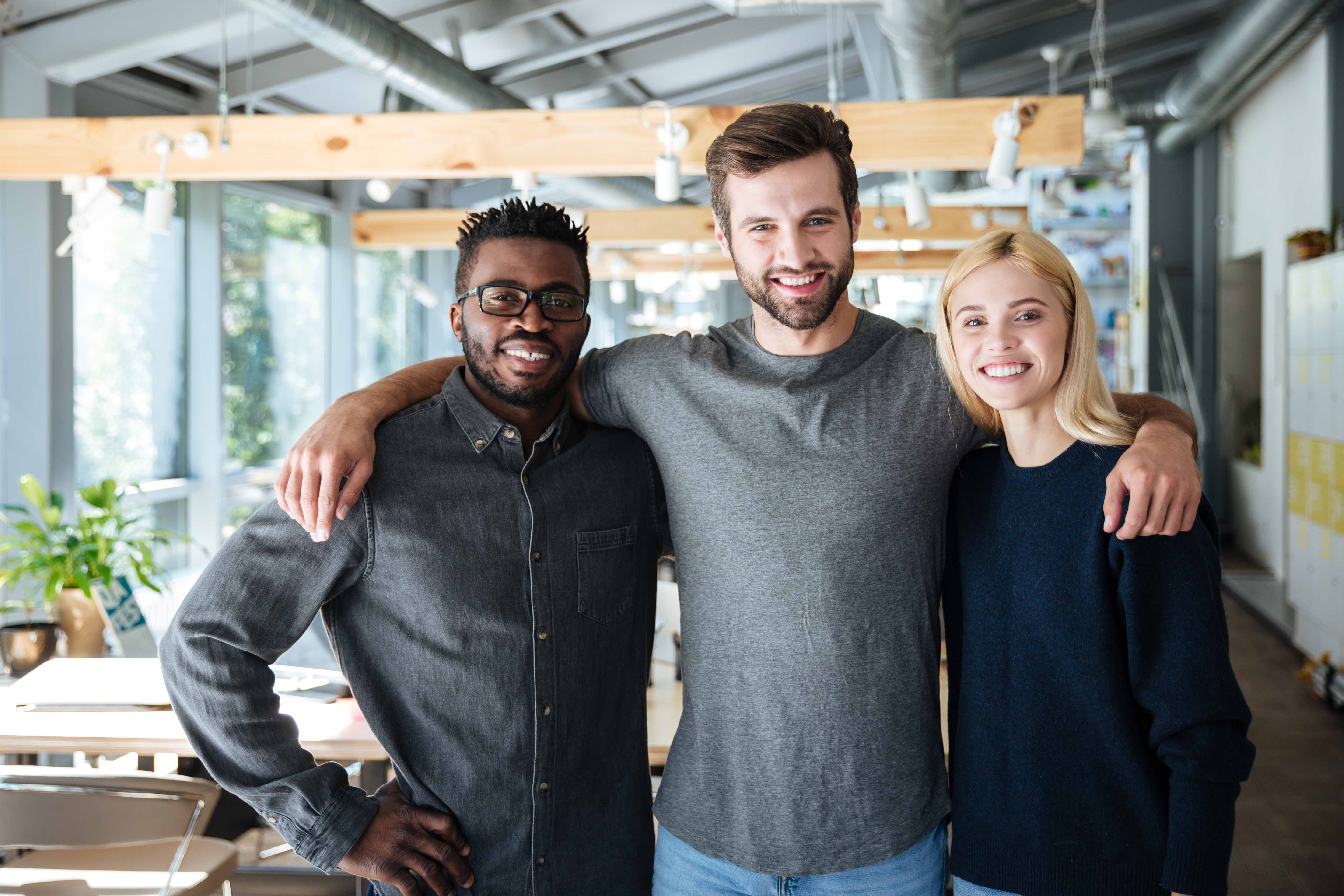 Image of smiling young colleagues standing in office. Looking at camera.