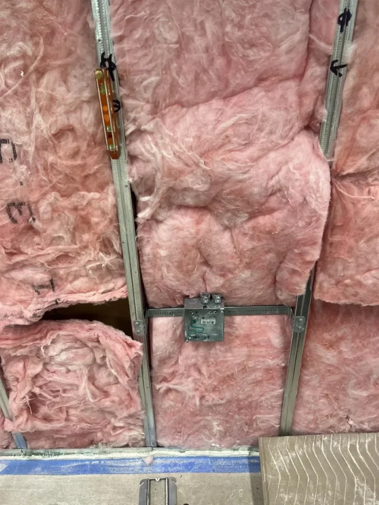 Open partition with acoustic insulation, metal studs, conduit, and an electrical box before close-in at Stantec Austin